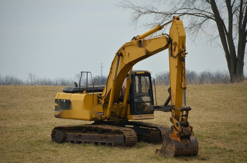 A mini excavator pulling stumps and brush on a partly cleared wooded lot