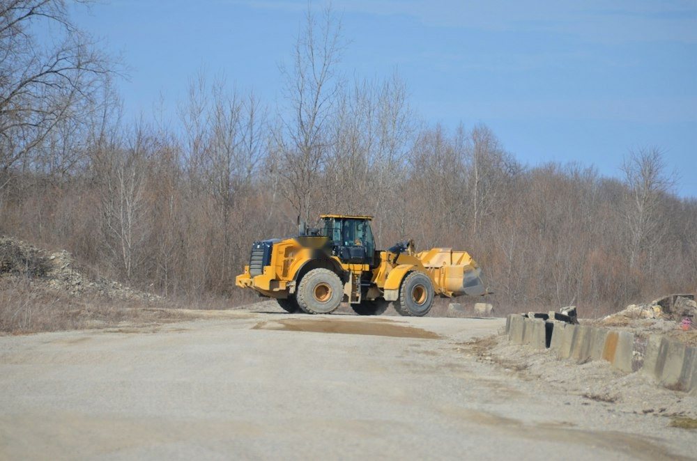 A compact track loader parked at the edge of a field beside a tree line